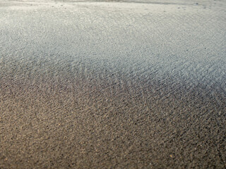  Black sand in the sun close-up. Quiet place. The silence of the waves Edge of the coast. Background from the sand. Black sand on the beach.