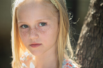 Beautiful little Caucasian girl with blue eyes, blond hair and freckles looking at the camera and...