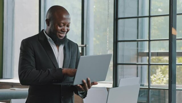African american man developer boss 30s senior businessman investor stand in office place hold portable laptop use touchpad to click on website programming code online trading search e-commerce data