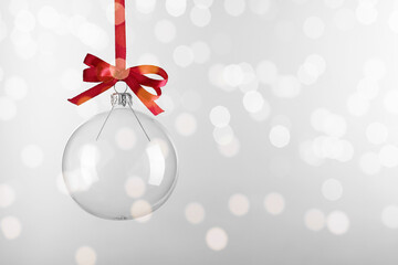 Transparent glass Christmas ball with red ribbon and bow against light background. Space for text