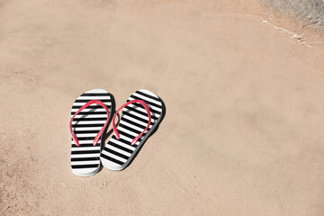 Fototapeta na wymiar Stylish flip flops on sandy beach near sea, space for text