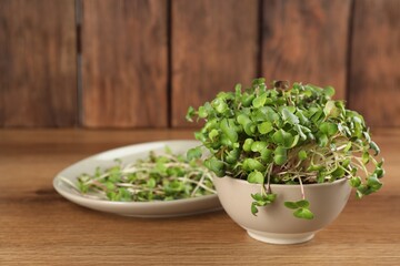 Fresh radish microgreens in bowl on wooden table, space for text