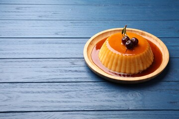 Delicious pudding with caramel and cherries on blue wooden table. Space for text