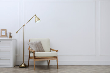 Stylish room interior with lamp, chest of drawers and armchair near white wall. Space for text