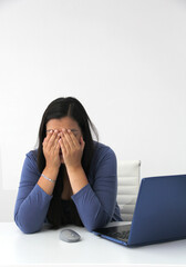 Dark-haired latin adult woman works in her office with laptop with a lot of stress having a headache with a migraine and suffering from tiredness, depression, anxiety and burnout