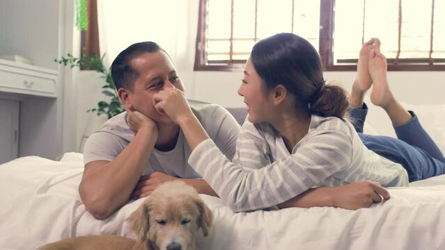 Cheerful young Asian family couple smiling bonding with his dog in the house. They give their little dog some love through a hug. Couples tease each other