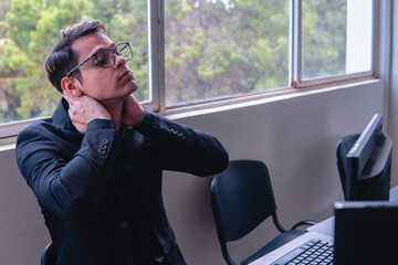 Tired office worker after a day of work. Man at a desk craning his neck. Office worker working on the computer at his desk. High quality photo