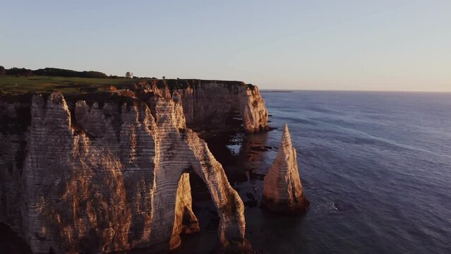 Beautiful coastal cliffs of bizarre shapes with natural arches and wild beaches in the rays of the setting sun. Etretat, France, cliffs on the banks of the English Channel, drone video
