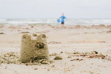 sand castle on the beach with a child and the ocean in the background on a cloudy day