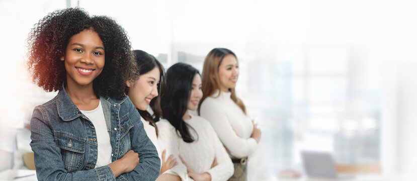 Portrait of young smiling woman looking at camera with crossed arms. Happy girl standing in office with her colleagues with copy space.