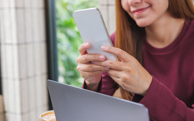Closeup image of a young woman holding and using smart phone and laptop computer in cafe