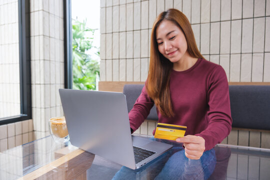 Portrait image of a young woman holding credit cards while using laptop computer for online payment