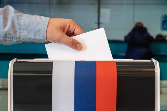 man putting electoral billuten in box during elections in russia. russia flag. voters to vote on a single voting day in Russia at a polling station