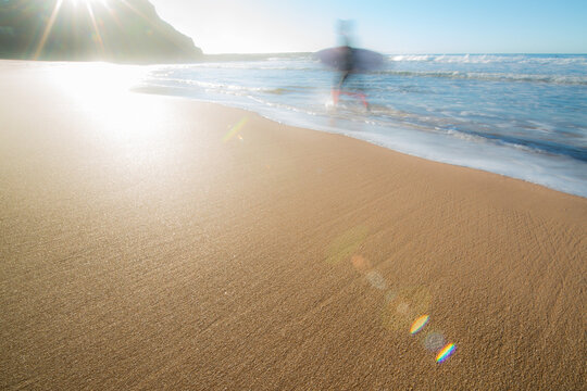 Surfer motion blur on yellow sandy beach with bright sun flare effects