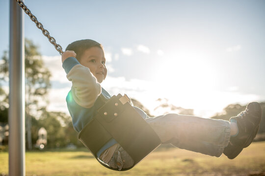 Cute mixed race three year old boy playing on a swing in a suburban playground