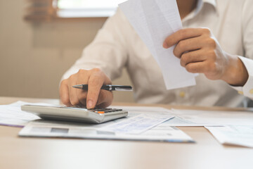 Fototapeta premium Close up hand of stress asian young businessman, male pressing a calculator to calculate tax income and expenses, bills, credit card for payment or payday at home, office.Financial, finance concept.