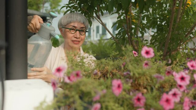 elderly Asian woman with a tattoo on her arm enjoy in watering plants