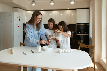 Happy family preparing food together in the kitchen. Mom teaches her daughters how to cook and knead the dough. Mother's Day concept. pour milk