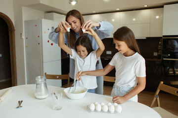 Obraz na płótnie Canvas Happy family preparing food together in the kitchen. Mom teaches her daughters how to cook and knead the dough. Mother's Day concept. break eggs