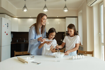 Happy family preparing food together in the kitchen. Mom teaches her daughters how to cook and knead the dough. Mother's Day concept. family dinner