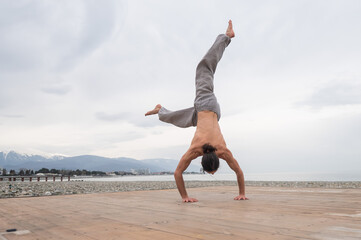 Fototapeta premium Shirtless caucasian man doing backflip on pebble beach. 