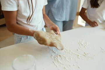 two little girls and their beautiful mother in aprons play and laugh while kneading dough in the...