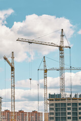 Industrial building cranes on background of cloudy sky. Hoisting cranes and multi-storey buildings of new city districts. Construction site background.