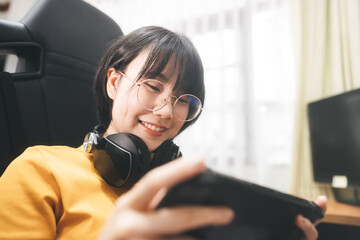Nerd style young adult asian gamer woman wear eyeglasses and headphone play a online game - obrazy, fototapety, plakaty