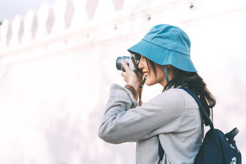 Young adult asian woman traveller wear blue hat and backpack travel in city using camera