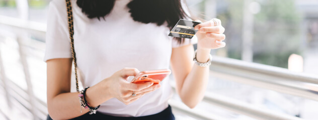 Adult woman consumer using creadit card and smartphone shopping via online application for spending money cashless.