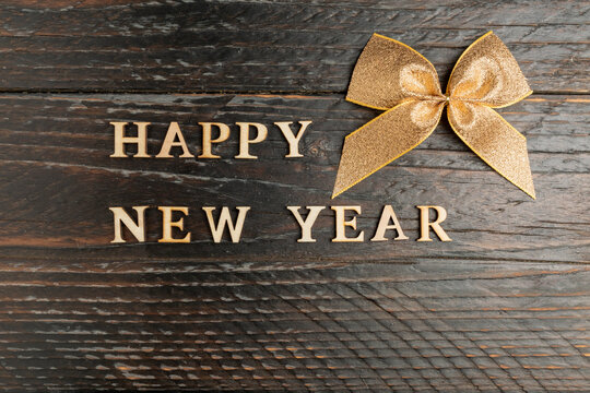 happy new year wooden text and golden bow on a wooden backgeound. Festive greeting card with copy space