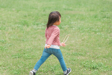 広い公園でおもちゃを持って走り回る子供（女の子・後ろ姿）
