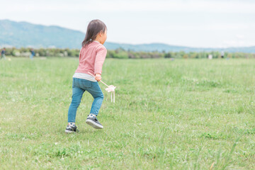 広い公園でおもちゃを持って走り回る子供（女の子・後ろ姿）
