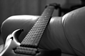 Grayscale of a guitar neck and fretboard on a sofa