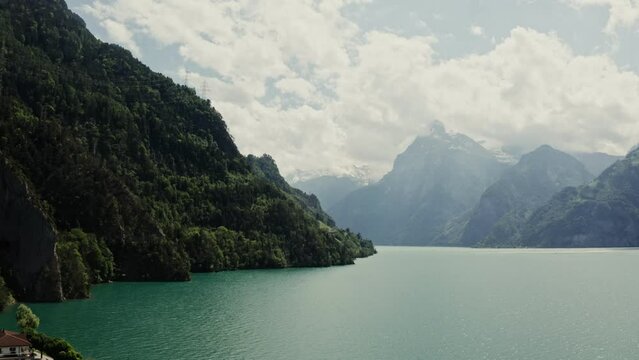 A picturesque lake in Switzerland between mountains overgrown with greenery, the tops of which are covered with white clouds. Lakeside town in the Alps, drone video