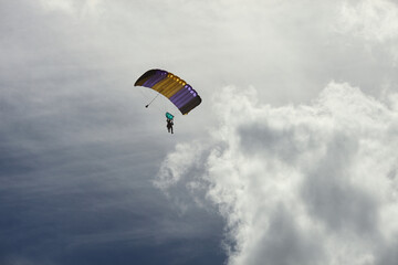 Skydiver silhouette under the parachute canopy against the sky with clouds.