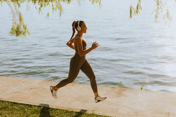 Active young beautiful woman running on the promenade along the riverside - obrazy, fototapety, plakaty
