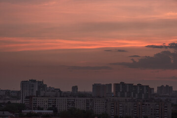 Fototapeta premium Sunset with gold, red, yellow and orange sunlight coming through the clouds, in a city among tall black houses. Horizontal photograph. Nature. Architecture.