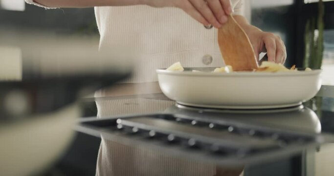 A woman fries potatoes on an induction electric stove with a built-in extractor fan