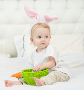 Little girl sitting on the bed in the bedroom with bunny ears on her head