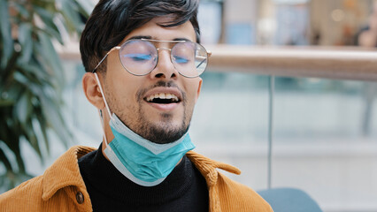 Close-up young hispanic guy takes off protective medical mask breathes fresh air taking deep breath...