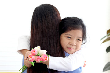 Adorable Asia happy smiling daughter girl giving beautiful tulip flowers for her mother and hugging her mom with love, warm love in family, Happy mother day, kid have special time with mom.