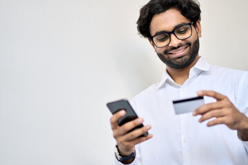 Smiling indian young business man buyer holding smartphone and credit card using cell phone mobile...