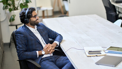 Young indian business man professional employee or executive manager wearing headphones sitting at...