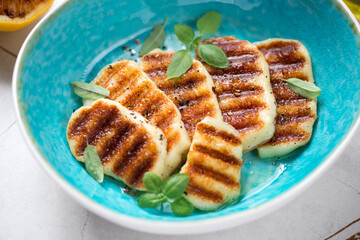 Turquoise bowl with slices of grilled haloumi cheese, close-up, selective focus, horizontal shot