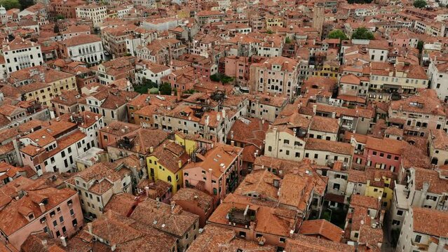 The drone flies over the orange rooftops of traditional Venetian houses. Narrow water channels instead of streets, aerial view, Italy