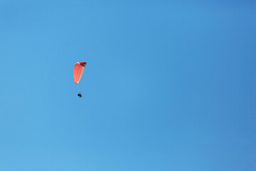 Red paraglider tandem instructor with a tourist flying into the sky with clouds on a sunny day