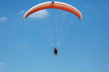 Red paraglider tandem instructor with a tourist flying into the sky with clouds on a sunny day