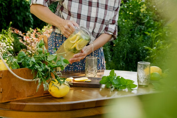 Woman pouring homemade lemonade beverage into glass in summer garden.