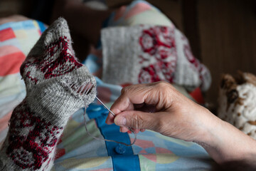 Close up of old lady hands darning winter socks with hole. Poverty in world economic crisis concept  - obrazy, fototapety, plakaty